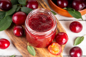 Cherry plum jam in small jar. Homemade autumn red cherry plum marmalade confiture with fresh fruits. Fall preparations, fruit preserves canning on wooden table background copy space