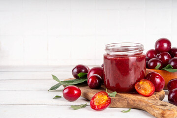 Cherry plum jam in small jar. Homemade autumn red cherry plum marmalade confiture with fresh fruits. Fall preparations, fruit preserves canning on wooden table background copy space
