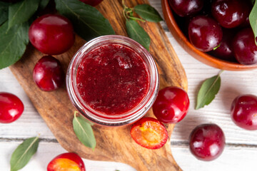 Cherry plum jam in small jar. Homemade autumn red cherry plum marmalade confiture with fresh fruits. Fall preparations, fruit preserves canning on wooden table background copy space