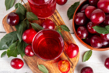 Sweet and tasty red cherry plum juice in in jug and glass, with fresh cherry plum fruits and tree...