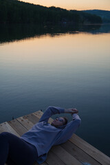 Woman lying down on the pier at lake, closeup portrait, summer sunset