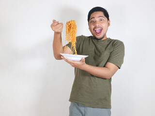Handsome Asian man holding a plate of fried noodles and showing a surprised expression. Eating...