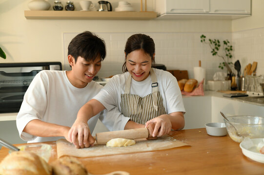 A Young man and woman bond over baking, working side by side to flatten dough. Joyful kitchen moment as couple teams up to prepare homemade cookies