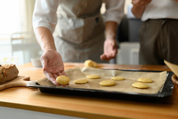 Close-up of hands placing round cookie dough pieces onto a baking tray lined with parchment paper