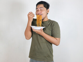 Handsome Asian man enjoying noodles with a fork while showing a delicious expression. eating lunch concept. isolated white background