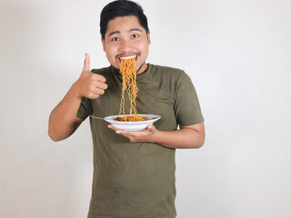 Handsome Asian man enjoying noodles, with the noodles still in his mouth, and giving a thumbs up....