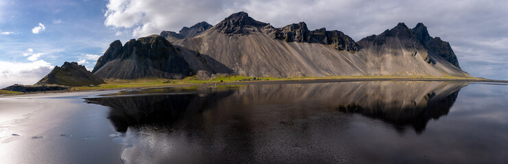 Vestrahorn mountain stands tall in Iceland, its rugged peaks mirrored in the tranquil dark waters...