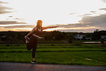 A plump young woman warms up before exercising for better health during sunset.