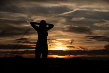 Silhouette of a plump young woman warming up before exercising for better health during sunset.