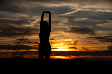 Silhouette of a plump young woman warming up before exercising for better health during sunset.