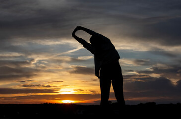 Silhouette of a plump young woman warming up before exercising for better health during sunset.