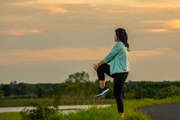 A plump young woman warms up before exercising for better health during sunset.