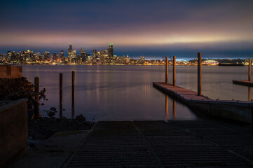 Fototapeta premium Sunrise Over The Seattle Skyline Across Elliott Bay. A calm early morning sunrise in the Pacific Northwest with beautiful clouds adding to the atmosphere. Don Armeni Boat Ramp in the foreground.