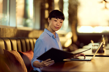 Professional Woman Researching and Working on a Laptop in a Cozy Café Setting