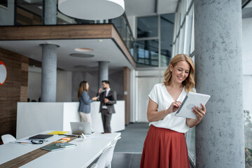 Smiling businesswoman using digital tablet in modern office lobby