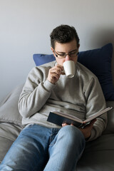 Young ma sitting on bed reading a book while having coffee