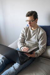 Teenager sitting on the bed using laptop, takes notes in a notebook