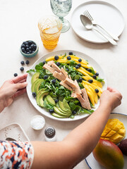 Woman serving fresh tuna salad with mango, avocado and blueberries