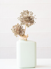 Dried allium flowers standing in a light green vase with raffia ribbon