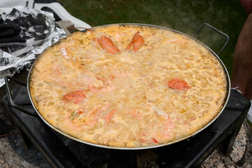 Chef cooking traditional paella with shrimps and lobster in large pan
