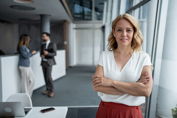 Confident businesswoman smiling with folded arms in modern office