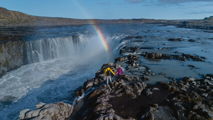 Visitors stand on rocky terrain, captivated by the majestic Selfoss waterfall in Iceland. A vibrant...