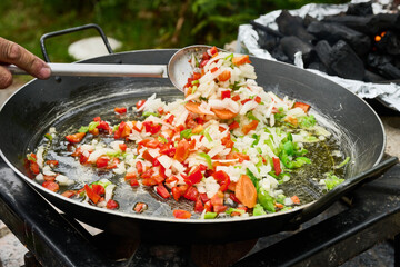 Chef adding chopped vegetables to paella pan over open fire