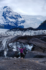 A traveler stands on the rugged terrain of Svinafellsjokull Glacier, marveling at the breathtaking...