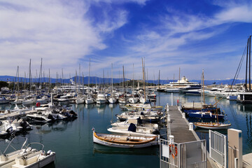 Fototapeta premium Marina with sailboats and yachts in Antibes on the Cote d'Azur with city walls and snow-capped mountains in the background, in spring