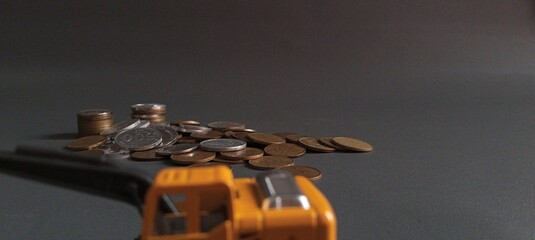 Blurred toy excavator in the foreground with focused stack of coins in the background, symbolizing financial effort and investment concept or the construction cost.