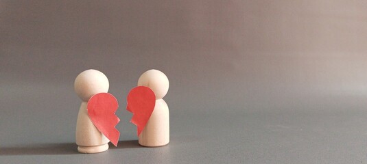 Two wooden peg dolls holding two broken halves of a red heart. Symbolizing heartbreak, separation,...