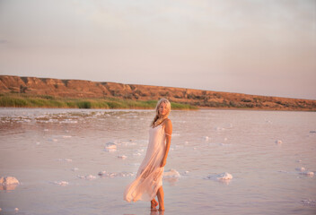 Mature graceful woman in airy dress standing in salt lake at sunset.  Calm contented with life with sweet happy smile