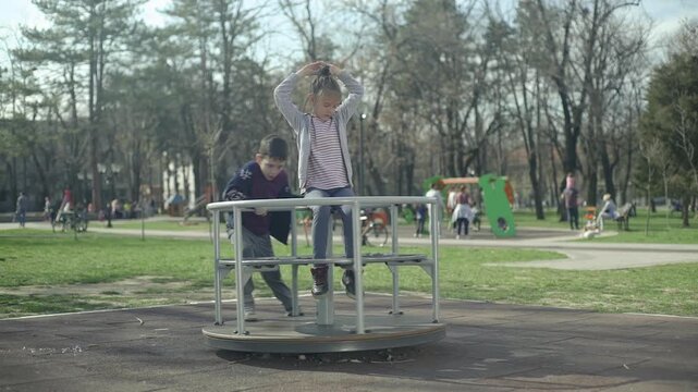 Kids are playing on the merry-go-round at the playground in the park during the spring season., slow-motion, medium shot,  shallow depth of field.