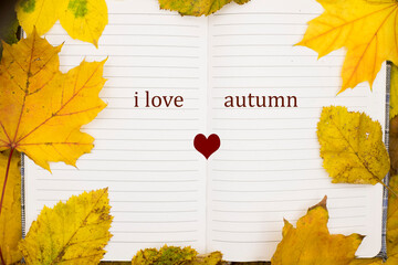 An open notebook displays the words I love autumn framed by vibrant yellow leaves, capturing the...