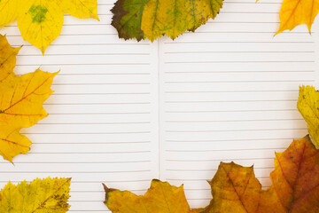 A notebook lies open with blank lines, bordered by colorful autumn leaves in shades of yellow,...