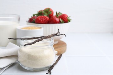 Different ingredients for panna cotta. Milk, sugar, vanilla and strawberries on white tiled table,...