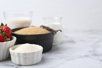 Different ingredients for panna cotta. Milk, sugar, vanilla and strawberries on white marble table,...