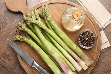 Fresh raw asparagus, spices, oil and knife on wooden table, top view