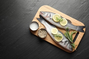 Fresh raw seabass fish with spices on black table, top view and space for text. Seafood delicacies