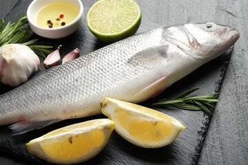 Fresh raw seabass with spices on black table, closeup. Fish and seafood delicacies