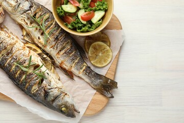 Tasty roasted seabass fish served with salad and lemon on white wooden table, top view and space for text. Homemade seafood dish