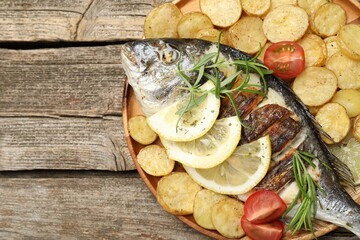 Tasty roasted dorado fish served with potatoes, tomatoes and lemon on wooden table, top view and space for text. Homemade seafood dish