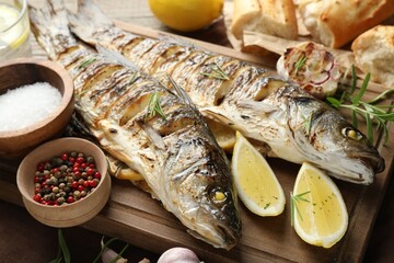 Tasty roasted seabass fish served with bread, rosemary and lemon on wooden table, closeup. Homemade seafood dish