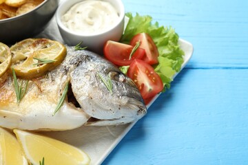 Tasty roasted dorado fish served with sauce on light blue wooden table, closeup. Space for text