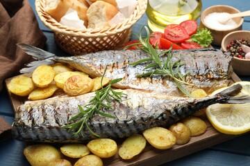 Tasty roasted mackerels served with spices and vegetables on blue wooden table, closeup. Homemade seafood dish
