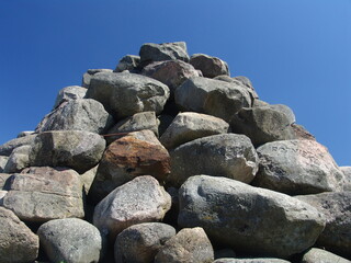 Pile of large, rugged boulders stacked under a clear blue sky, showcasing natural textures and outdoor geological formations.