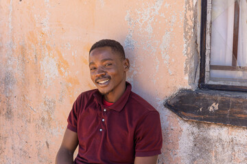 Africa village, single smiling young african men resting in front of the house, window and wall