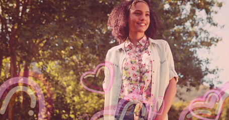 Smiling woman wearing pastel floral shirt and headband in sunlit park, with heart rainbow overlays