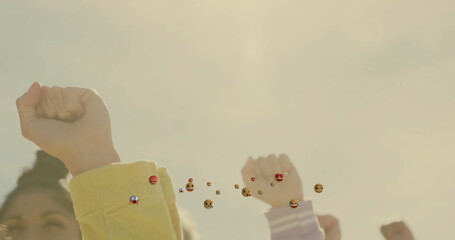 Raising fists women wearing colored sleeves uniting in outdoor space with floating reaction emojis