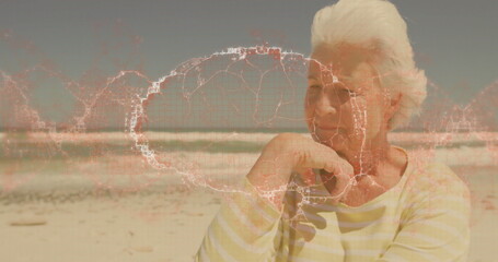 Sitting senior woman leaning on hand at sandy beach, with network map overlay, copy space